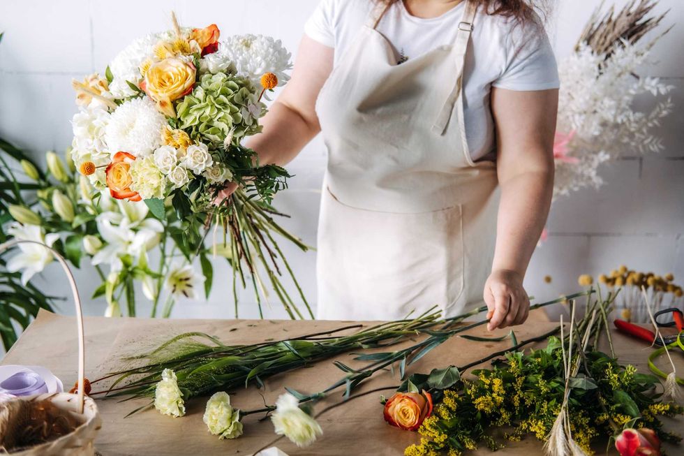 Florist arranging a bouquet with roses and hydrangeas at a wooden table.