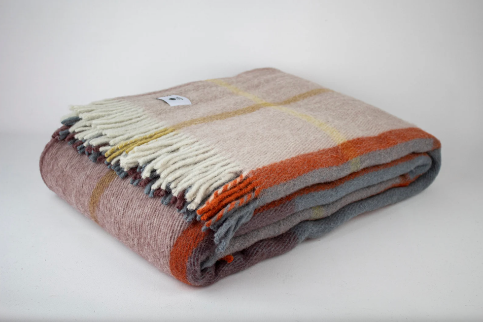 Folded plaid blanket with fringe, in earth tones on a white surface.