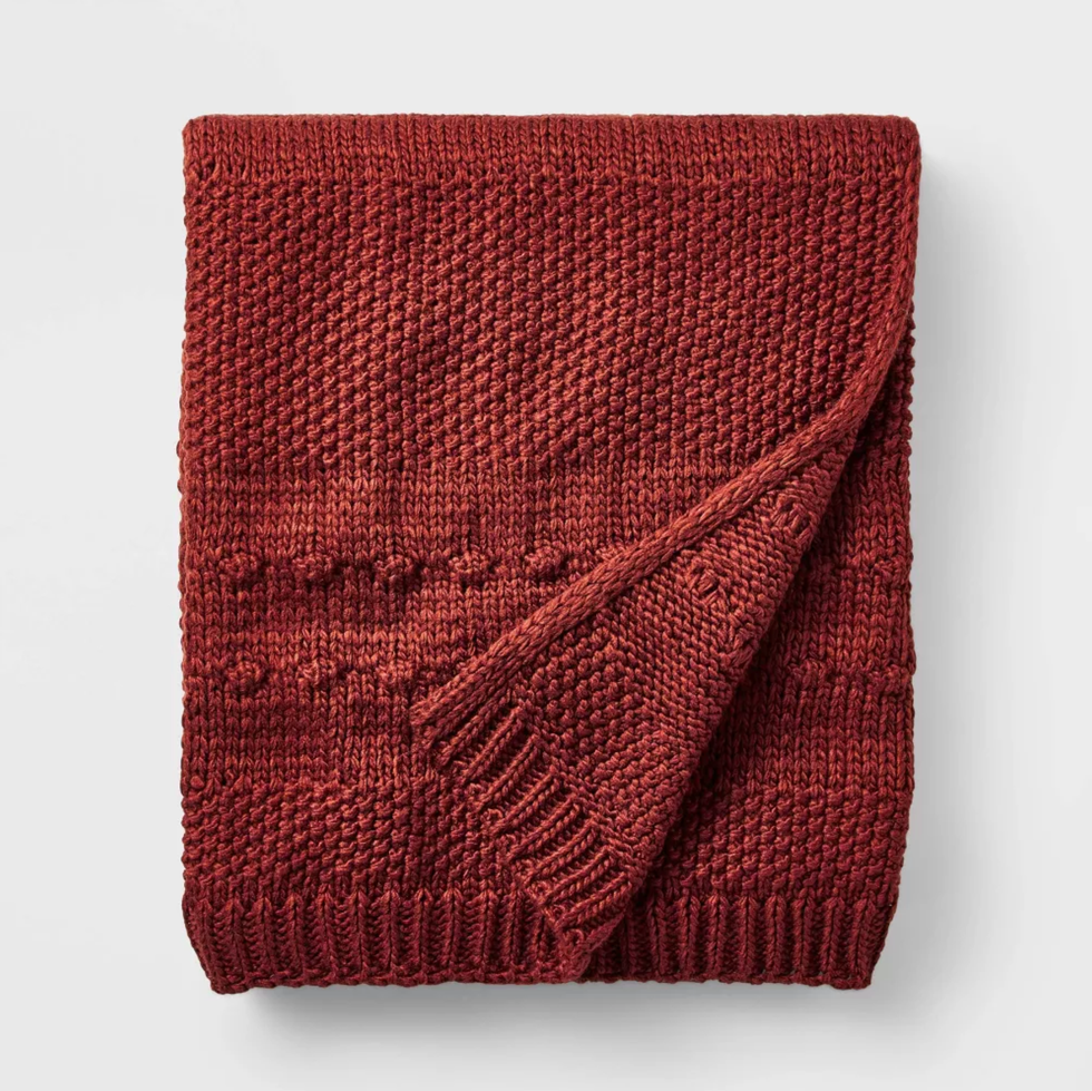 Folded red knitted blanket with textured patterns on a white background.