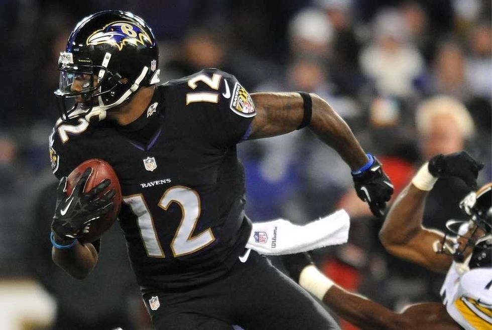 Football player in black Ravens jersey evades tackle, holding a football, during a game.