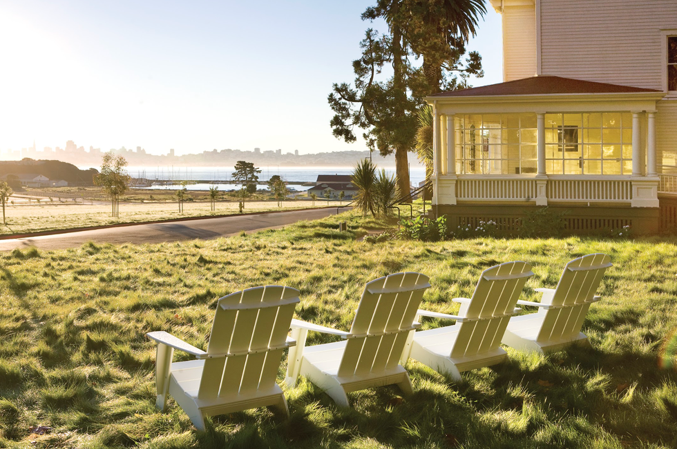 Four chairs on a sunny lawn overlook a bay and distant cityscape.