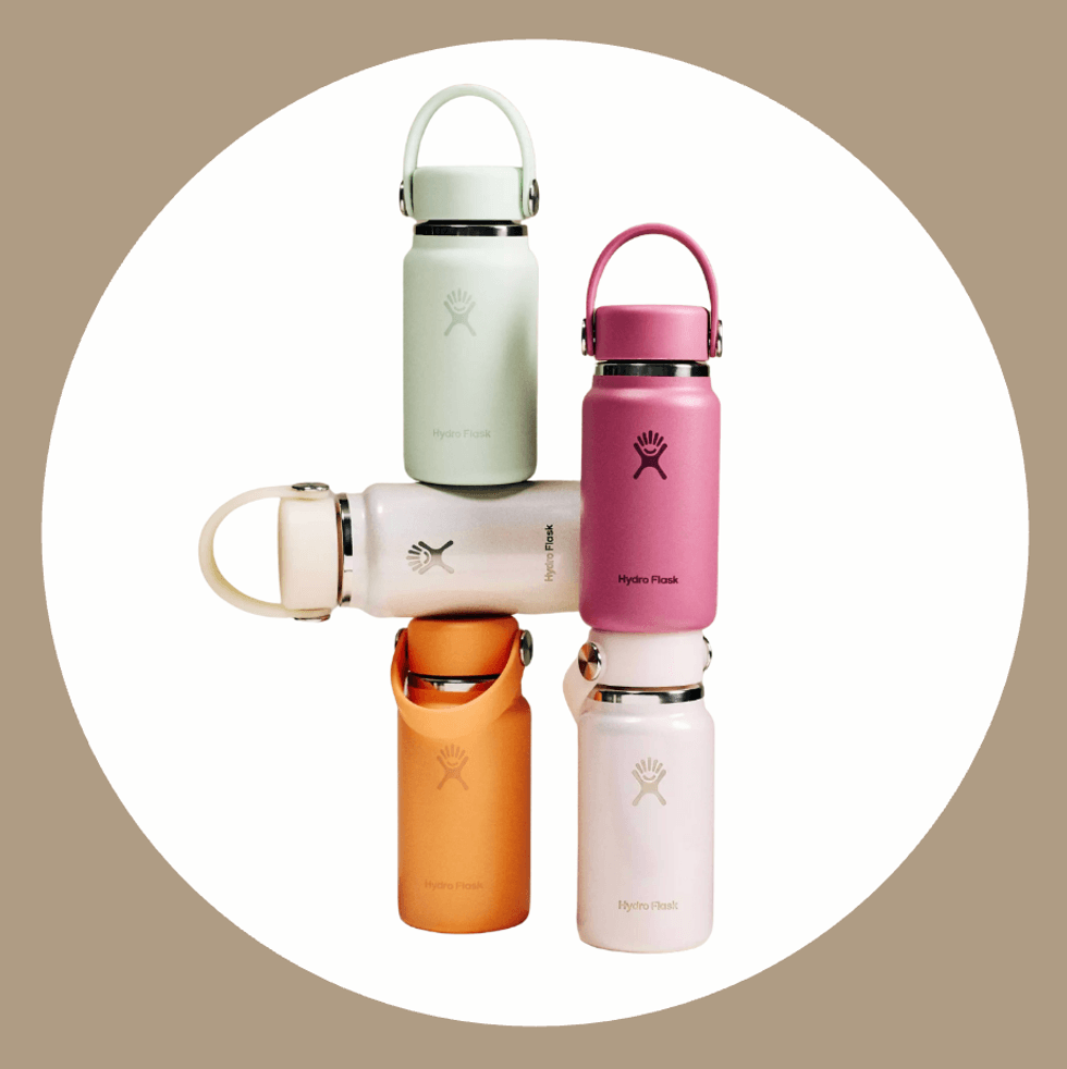Four colorful Hydro Flask bottles stacked creatively on a beige background.