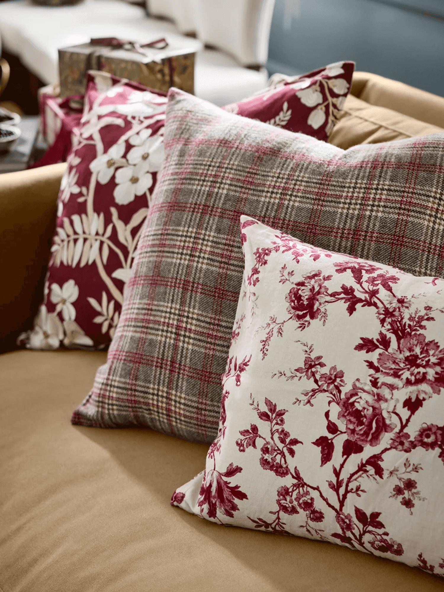 Four decorative pillows with floral and plaid patterns on a beige couch.