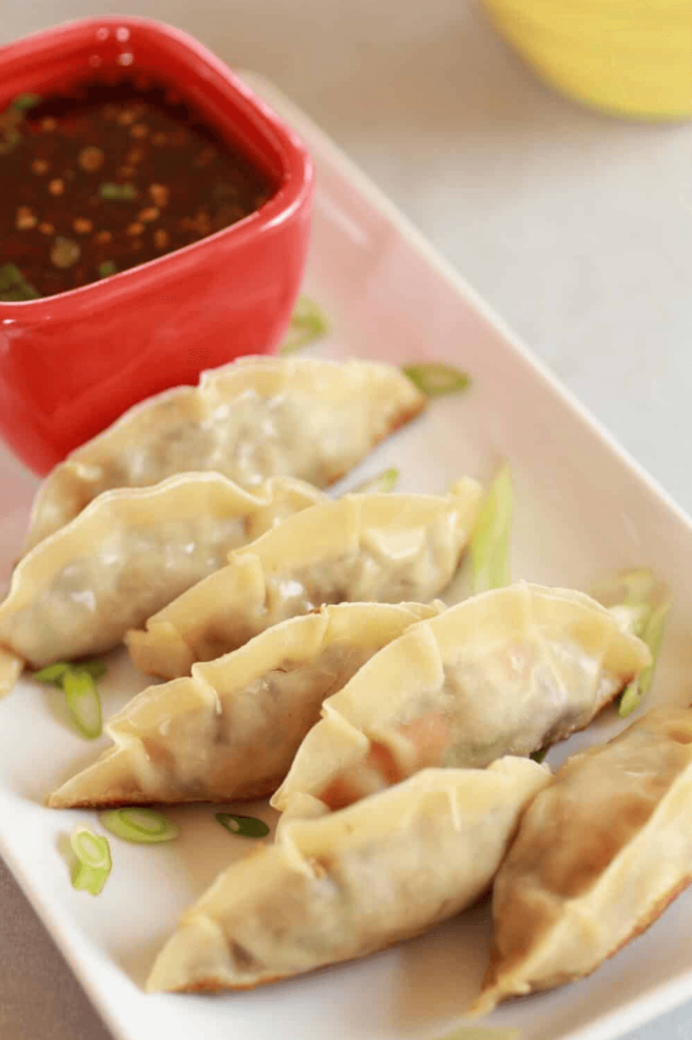 Four dumplings with dipping sauce on a white rectangular plate.