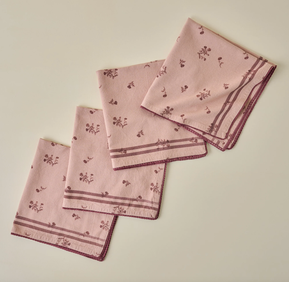 Four folded pink napkins with floral patterns and striped edges.
