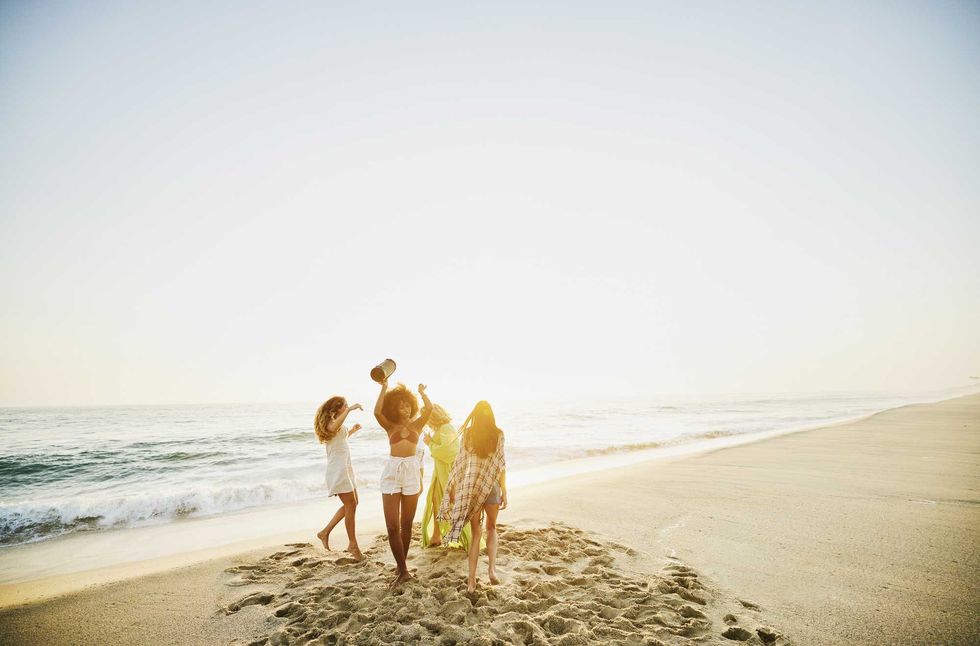 Four friends enjoying a sunset on the beach, standing near the water.