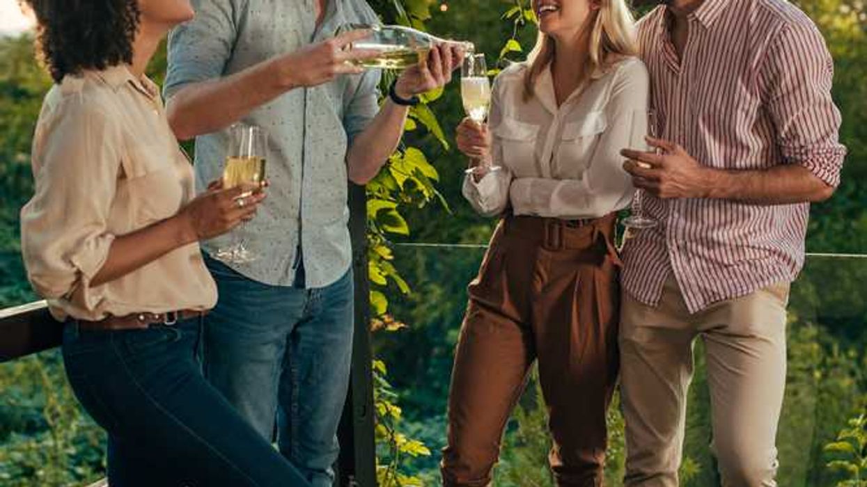 Four friends enjoying drinks on a vine-covered deck at sunset.
