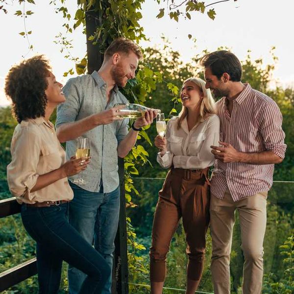 Four friends enjoying drinks on a vine-covered deck at sunset.