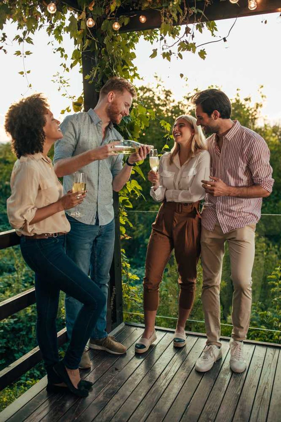 Four friends enjoying drinks on a vine-covered deck at sunset.