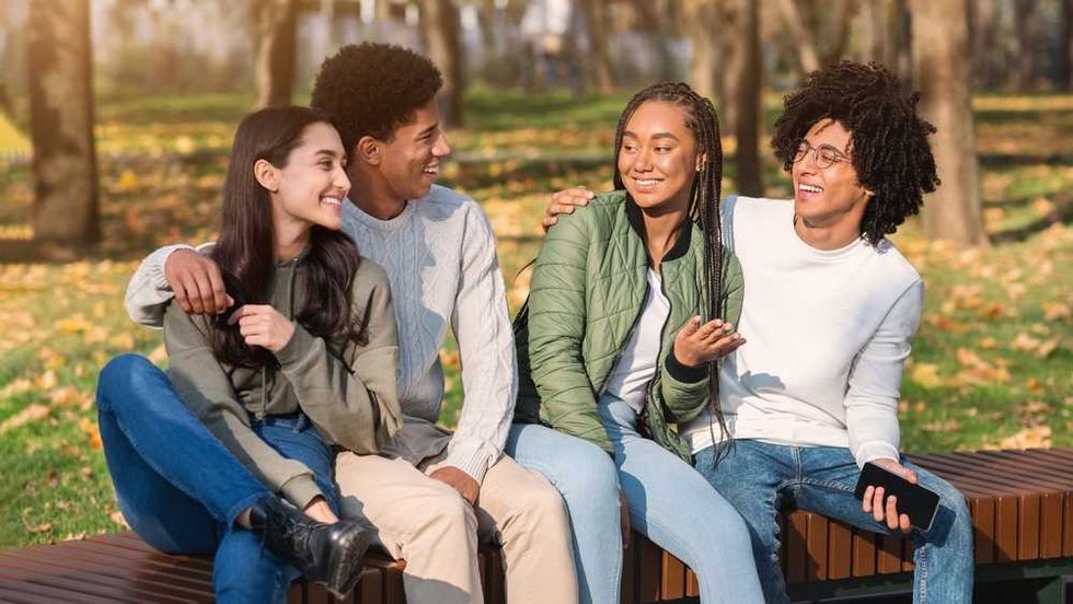 Four friends laughing and chatting on a park bench in autumn.