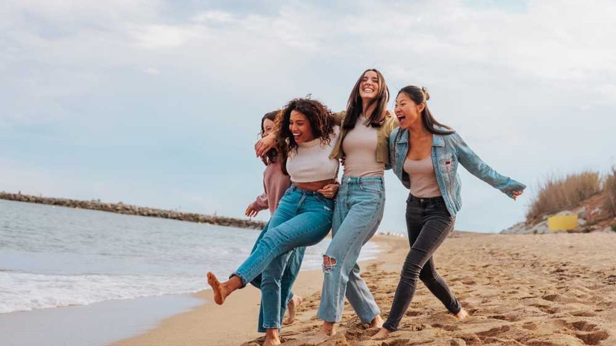 Four friends laughing and walking on a sandy beach.
