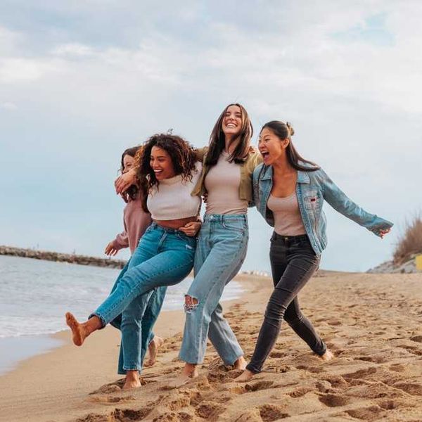 Four friends laughing and walking on a sandy beach.