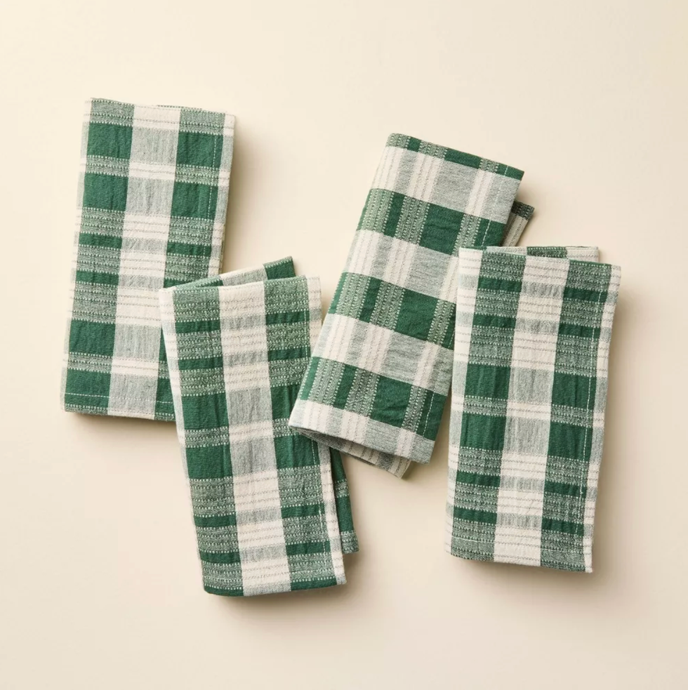 Four green and white plaid napkins on a beige surface.
