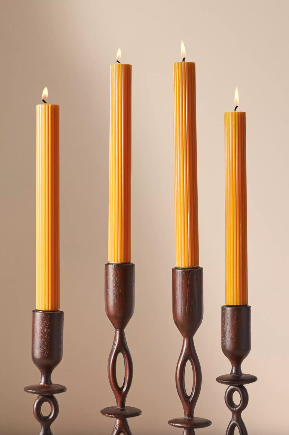 Four lit yellow candles in wooden holders on a neutral background.