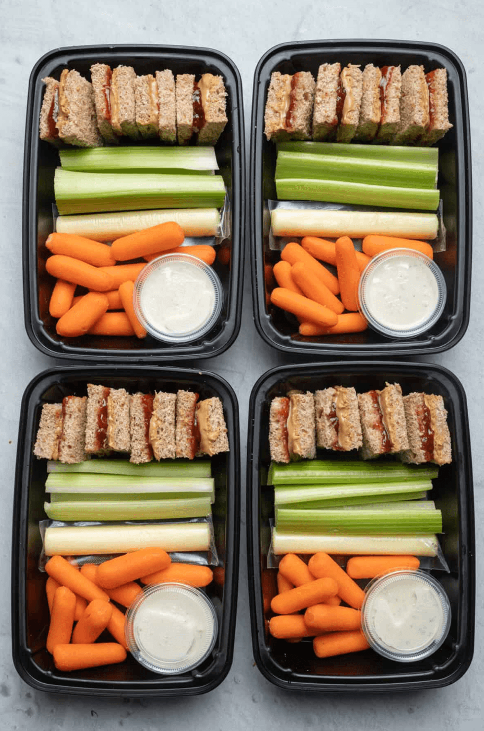 Four meal prep boxes with sandwiches, celery, carrots, string cheese, and ranch dip.