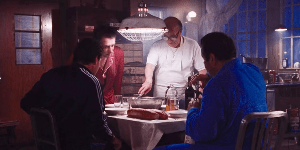 Four men in a dimly lit kitchen sharing a meal around a table.
