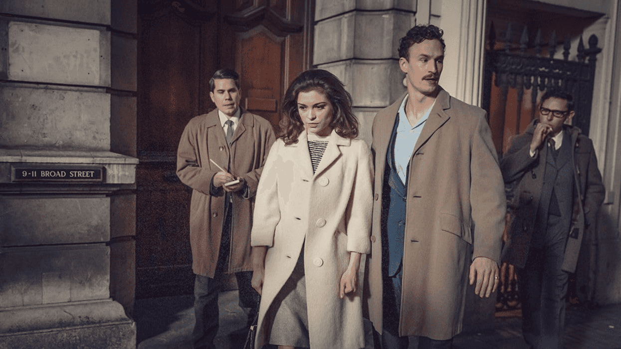 Four people in vintage coats walking on a city street at night.
