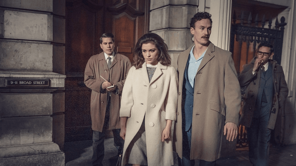 Four people in vintage coats walking on a city street at night.