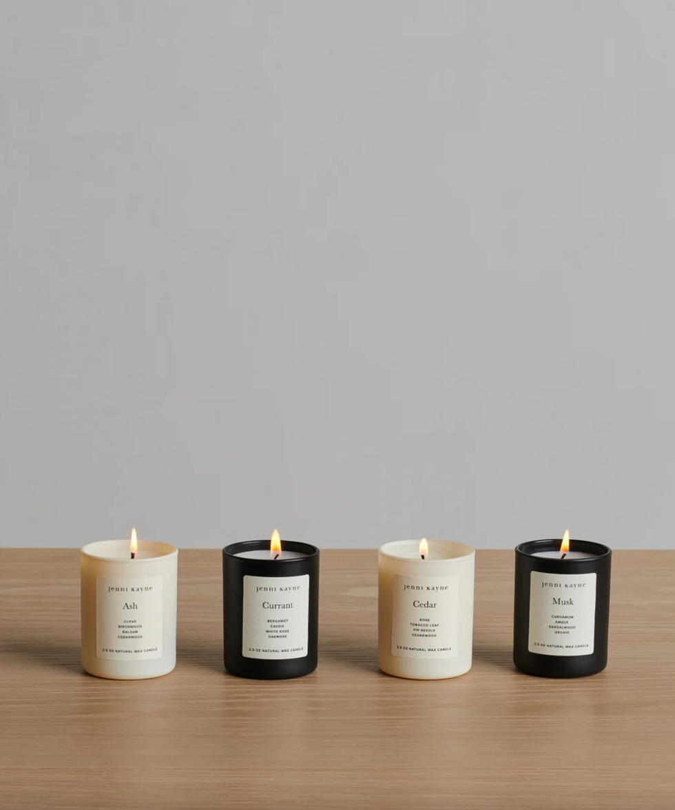 Four scented candles on a table, two white and two black, with labels facing forward.