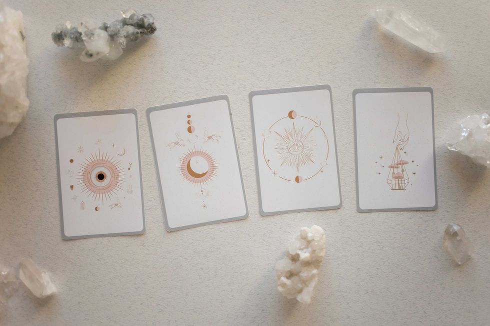 Four tarot cards with mystical designs surrounded by crystals.
