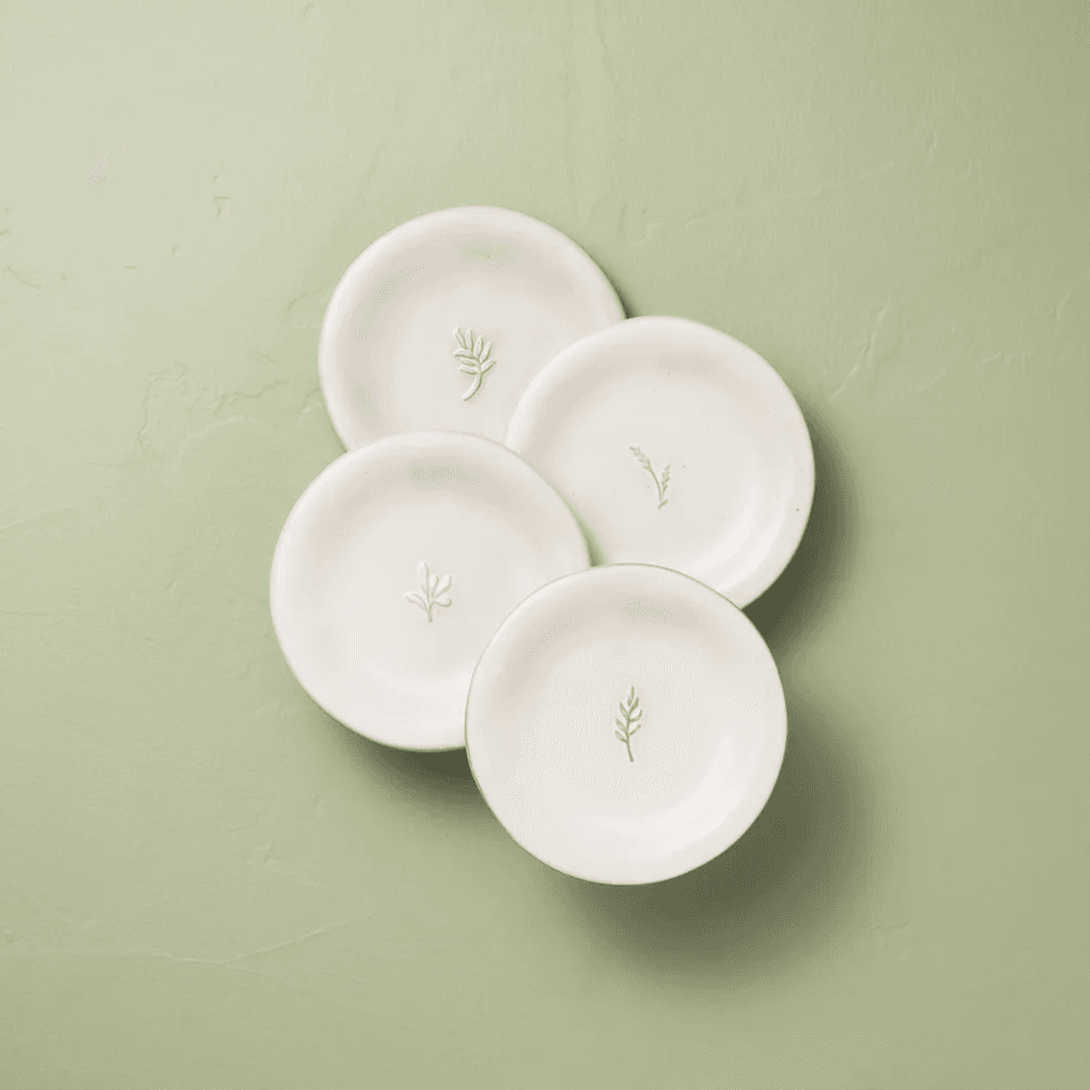 Four white ceramic plates with leaf imprints on a light green background.