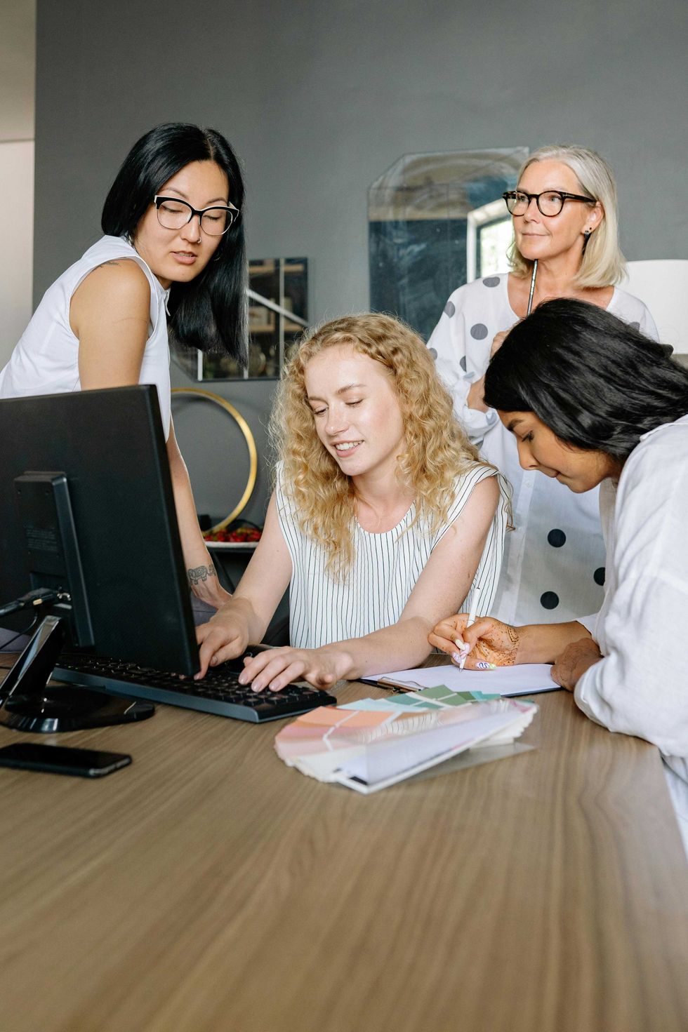 Four women collaborating at a desk with a computer and documents.