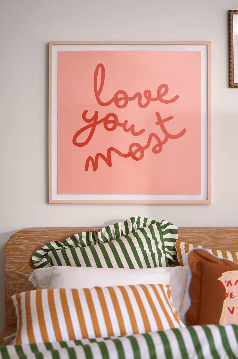 Framed "love you most" poster above a bed with colorful striped pillows.