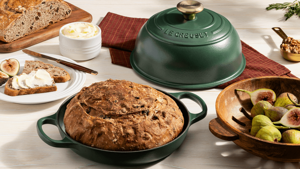 Freshly baked bread in a green Dutch oven, with figs, butter, and walnut garnish.