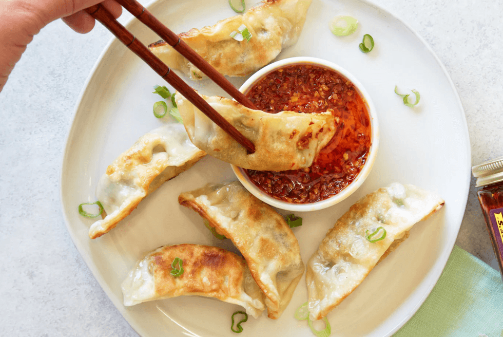 Fried dumplings with chili sauce on a plate, one being held by chopsticks.