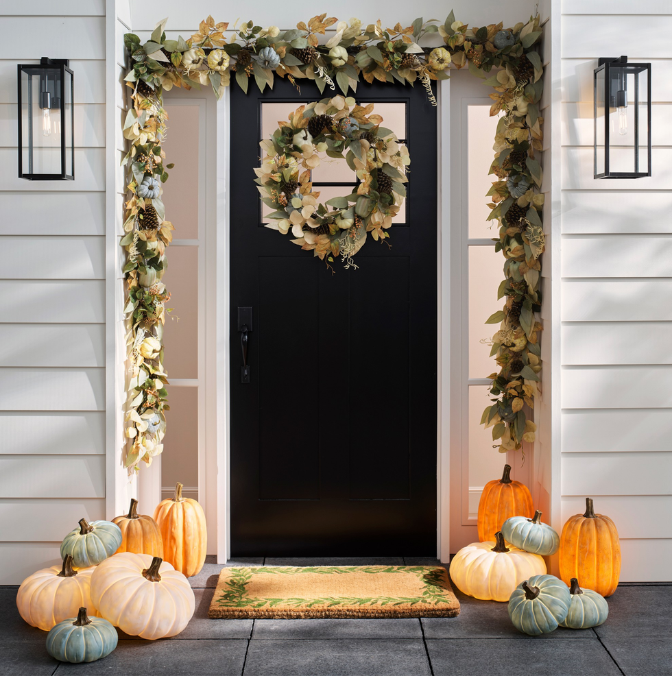 Front door with autumn wreath, garland, and assorted pumpkins on porch.