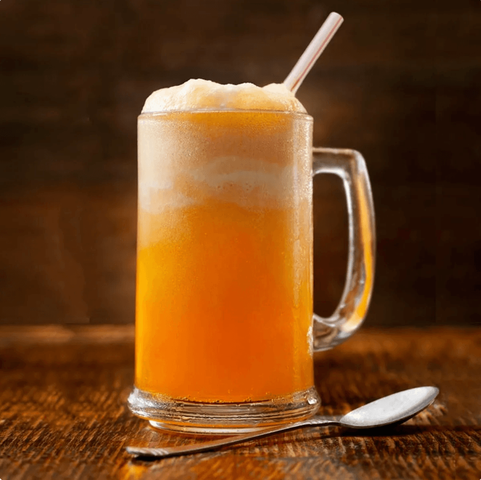 Frosty mug of orange soda float with a straw, next to a spoon on a wooden table.
