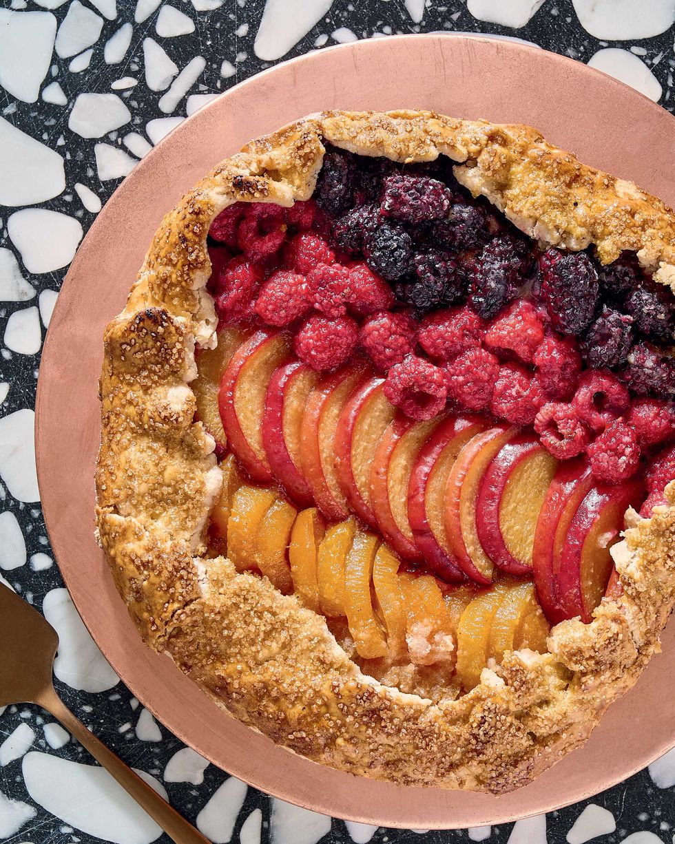 Fruit tart with berries and sliced peaches on a textured black and white surface.