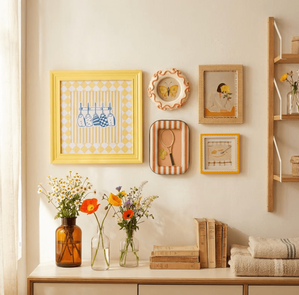 Gallery wall with colorful frames, vases of flowers, vintage books, and folded towels.