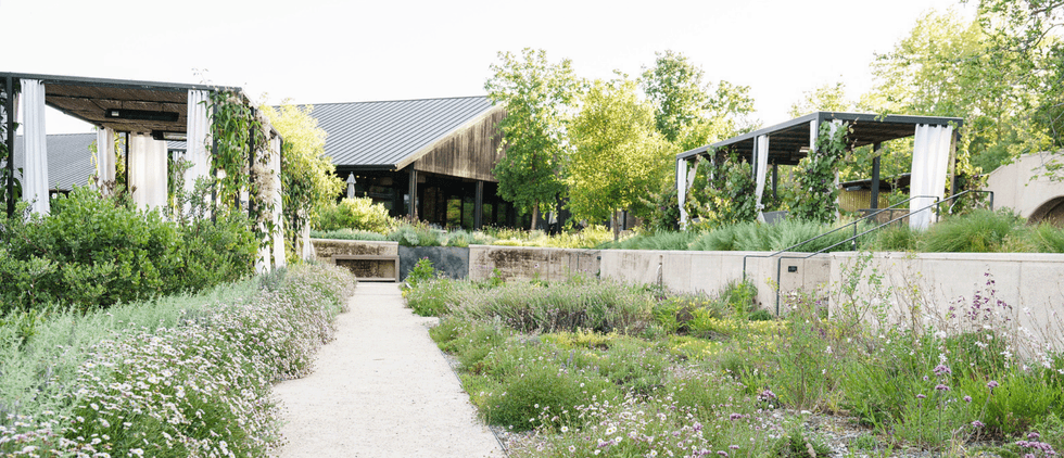 Garden path flanked by greenery and open structures under a bright sky.