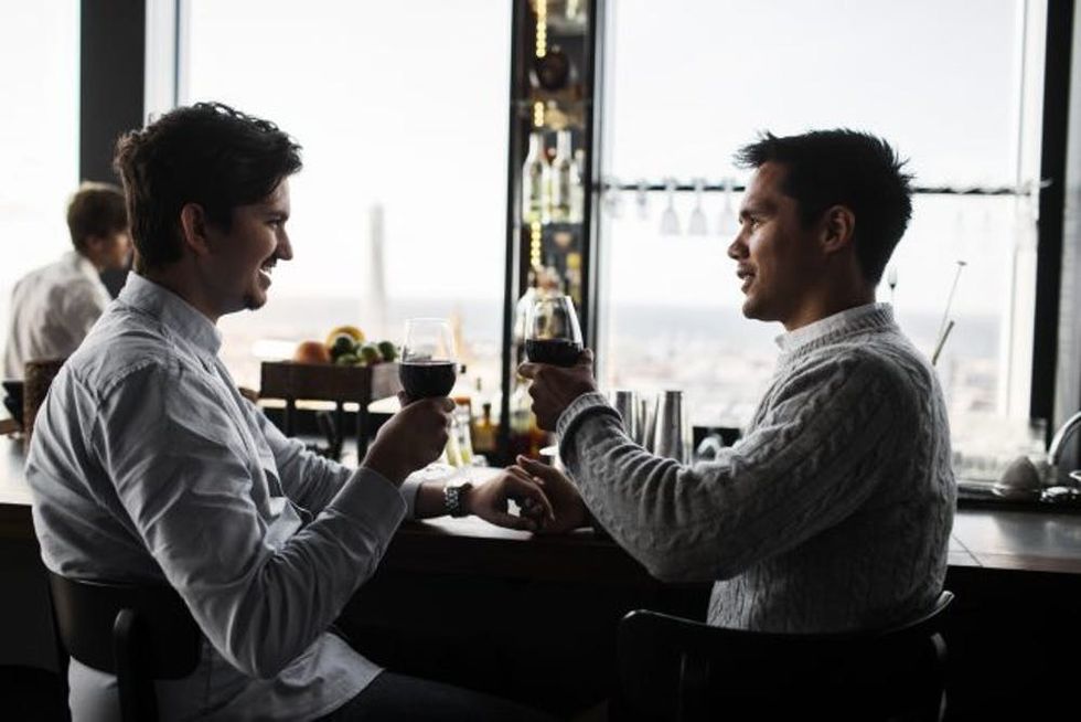 Gay couple toasting with red wine at table in sky bar restaurant