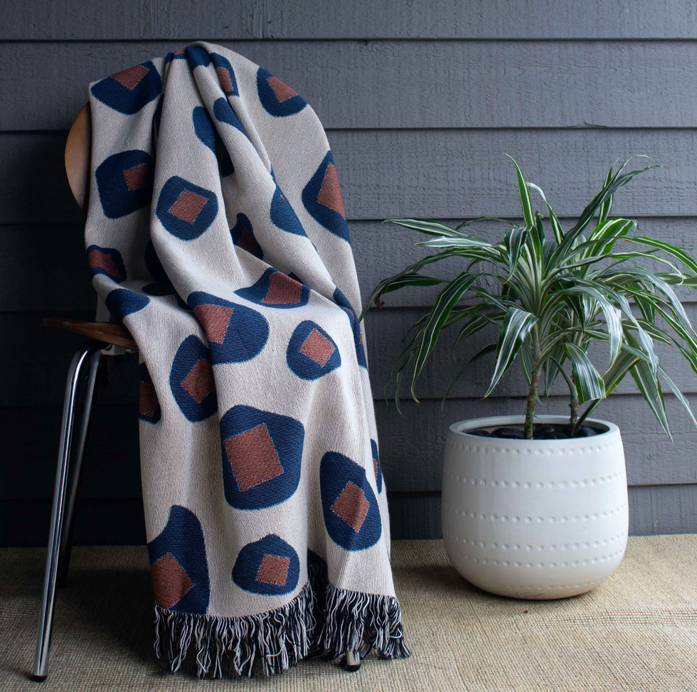 Geometric-patterned blanket on chair beside potted plant.