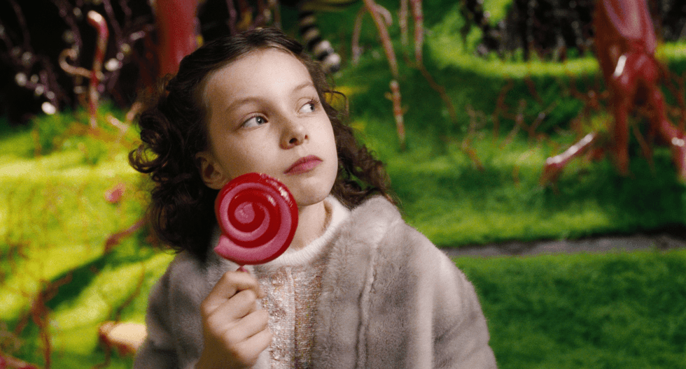 Girl holding a red lollipop in a whimsical garden setting.