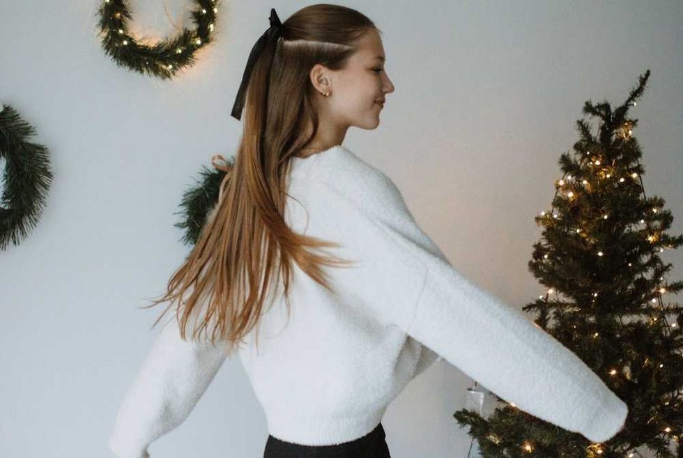 Girl in a white sweater twirls near a decorated Christmas tree and wreaths.