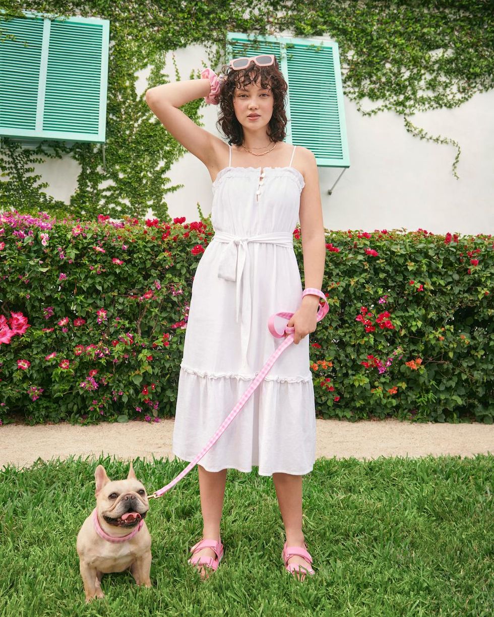 girl in white dress stand with her dog on a pink gingham leash