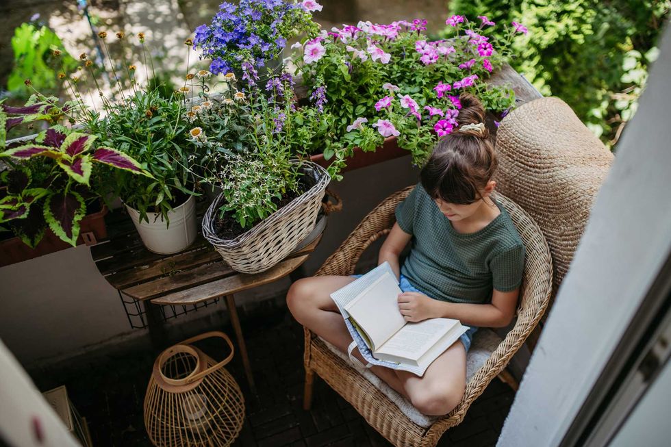 Girl reading on a cozy balcony with vibrant flowers and plants.