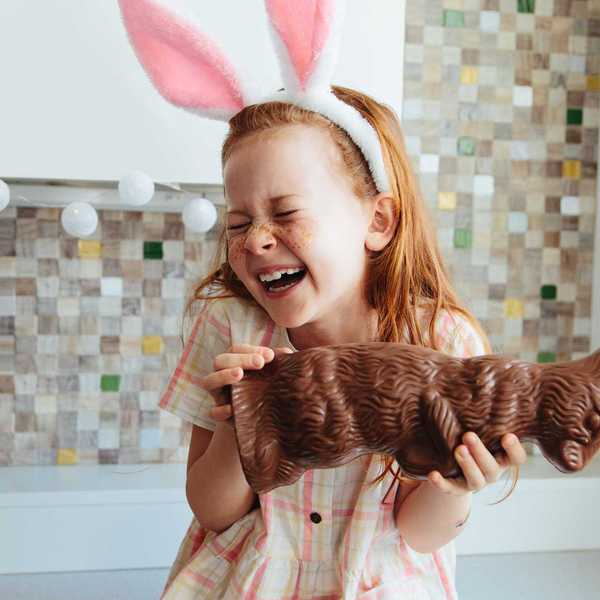 Girl with pink bunny ears laughs holding a large chocolate rabbit.