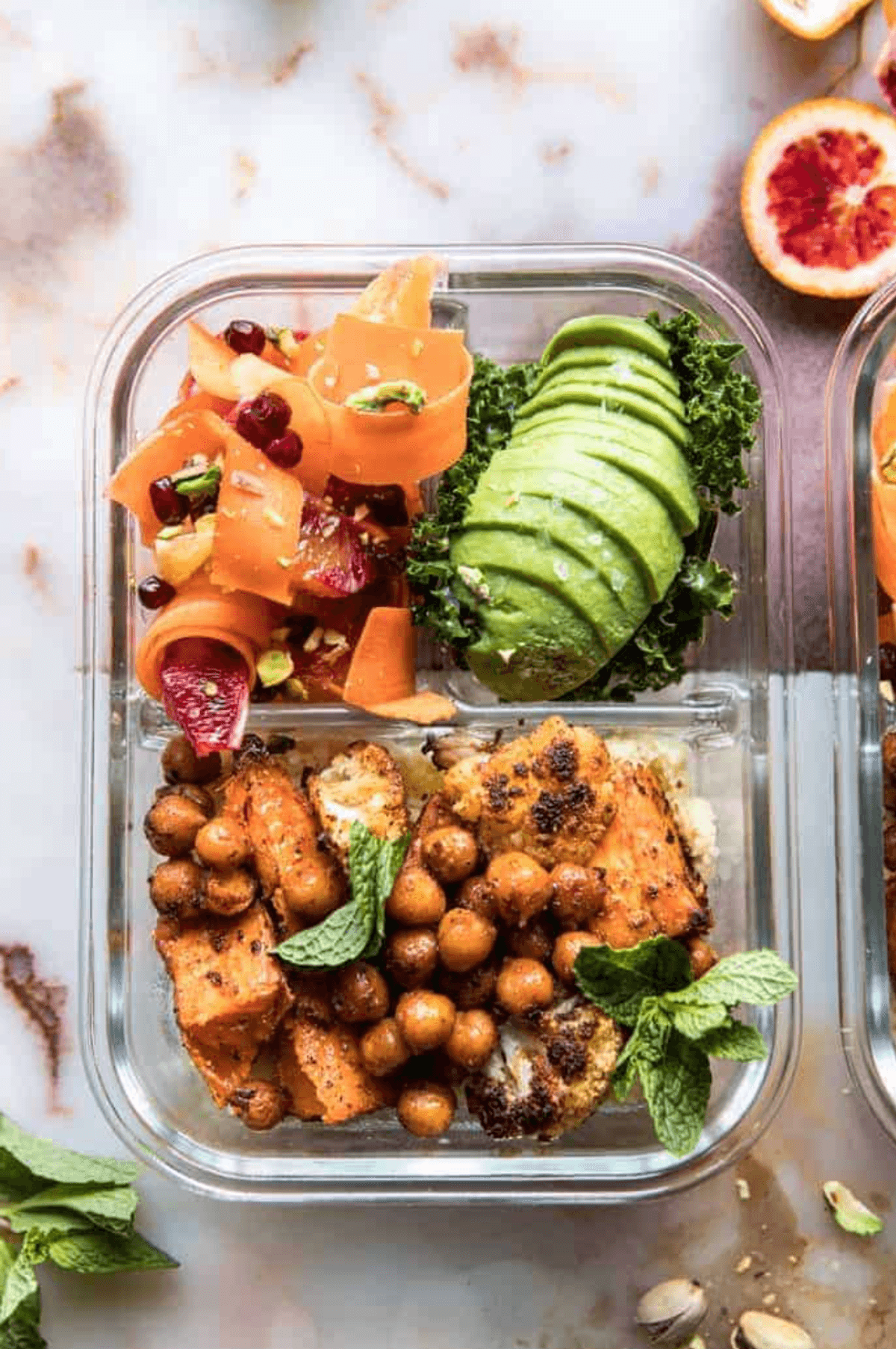 Glass container with chickpeas, avocado, carrot salad, and mint garnish.