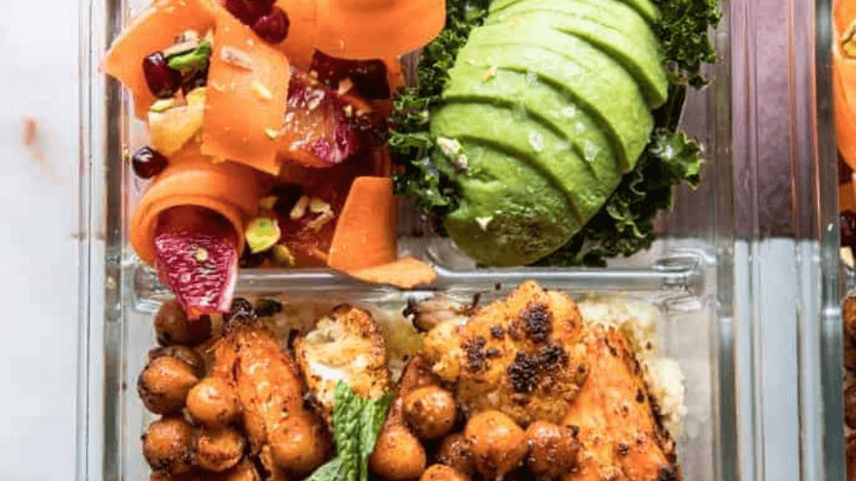 Glass container with chickpeas, avocado, carrot salad, and mint garnish.