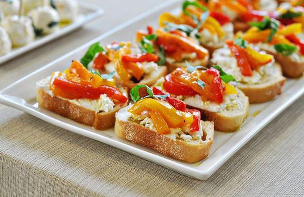 goat cheese with red and yellow roasted peppers and basil on top of a baguette