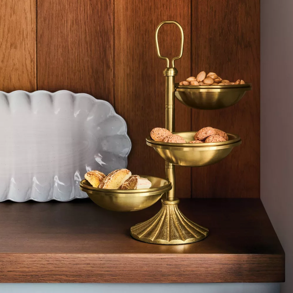 Gold-tiered tray with cookies and nuts on a wooden shelf.