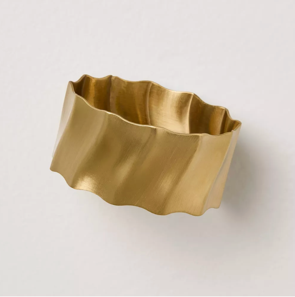 Gold-toned, wavy-edged circular metal napkin ring on a plain background.