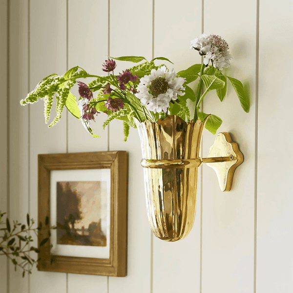 Gold wall vase with assorted flowers on a paneled wall.
