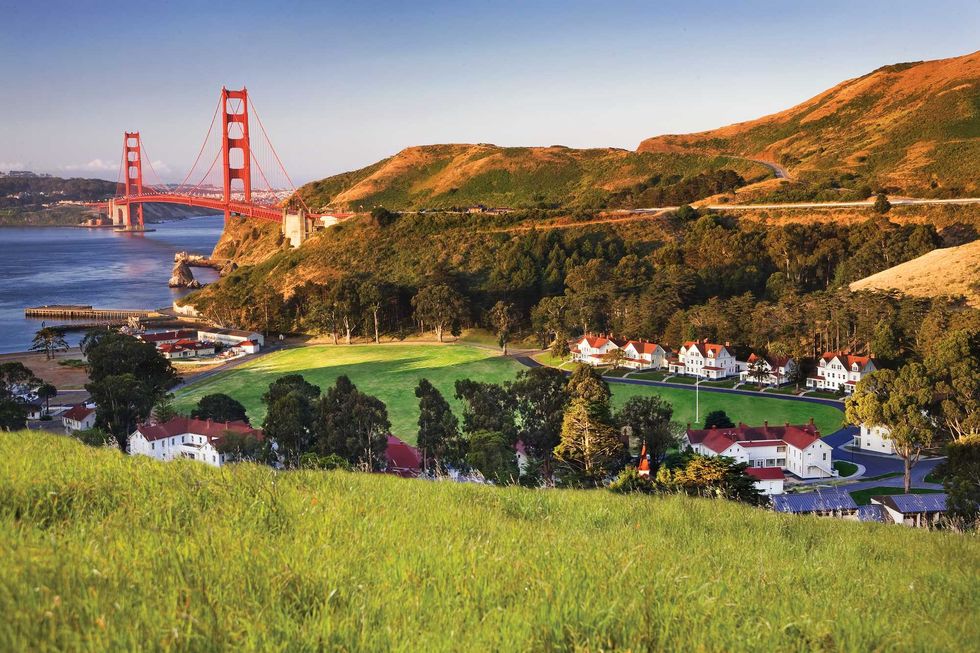 Golden Gate Bridge with grassy hills and buildings at sunset.