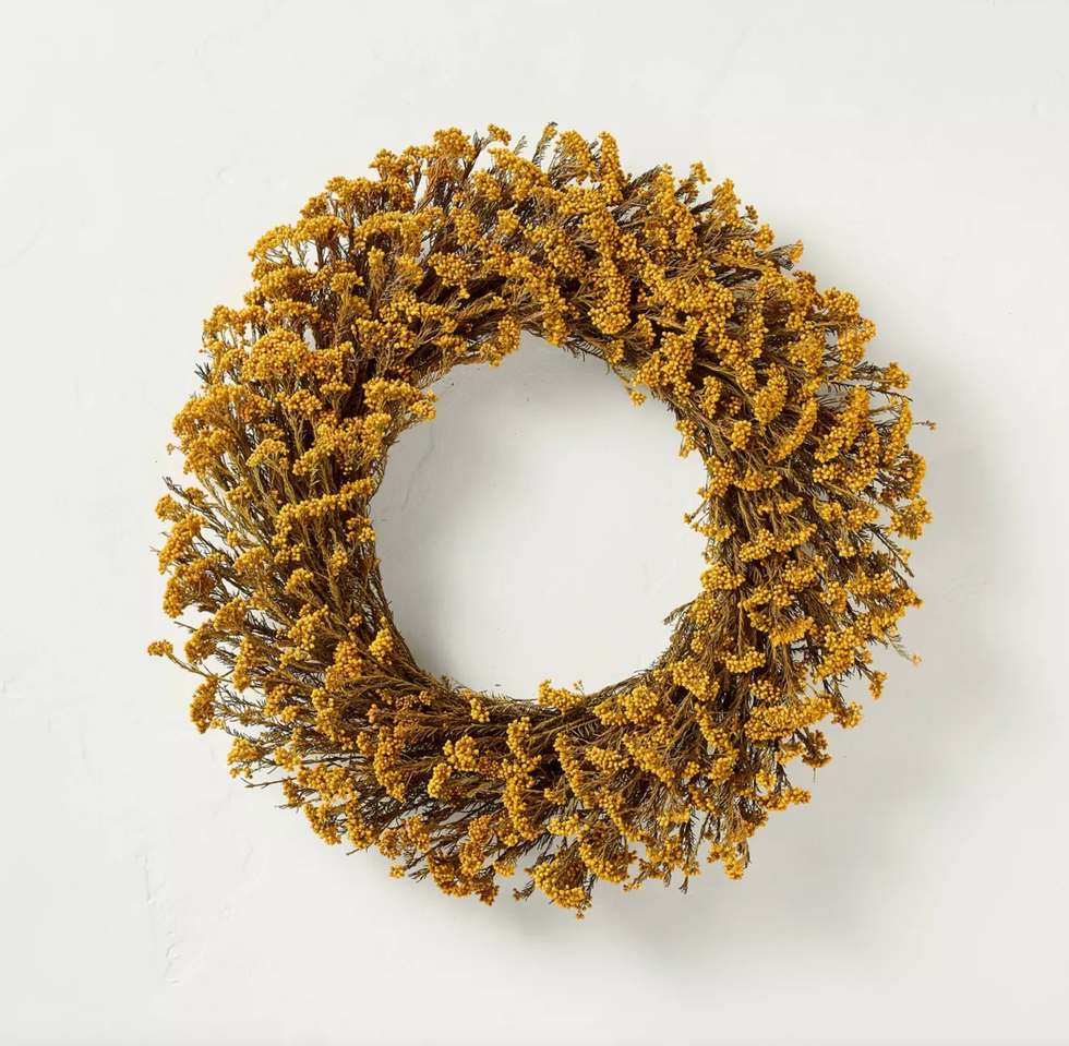 Golden-yellow dried floral wreath hanging on a white wall.