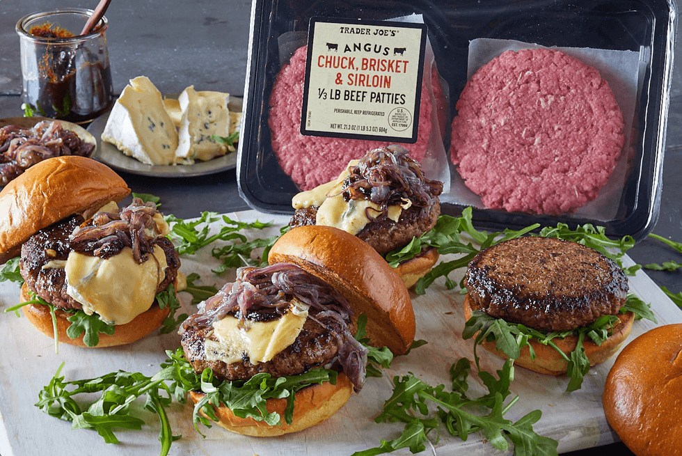 Gourmet burgers with cheese, onions, and arugula next to raw beef patties.